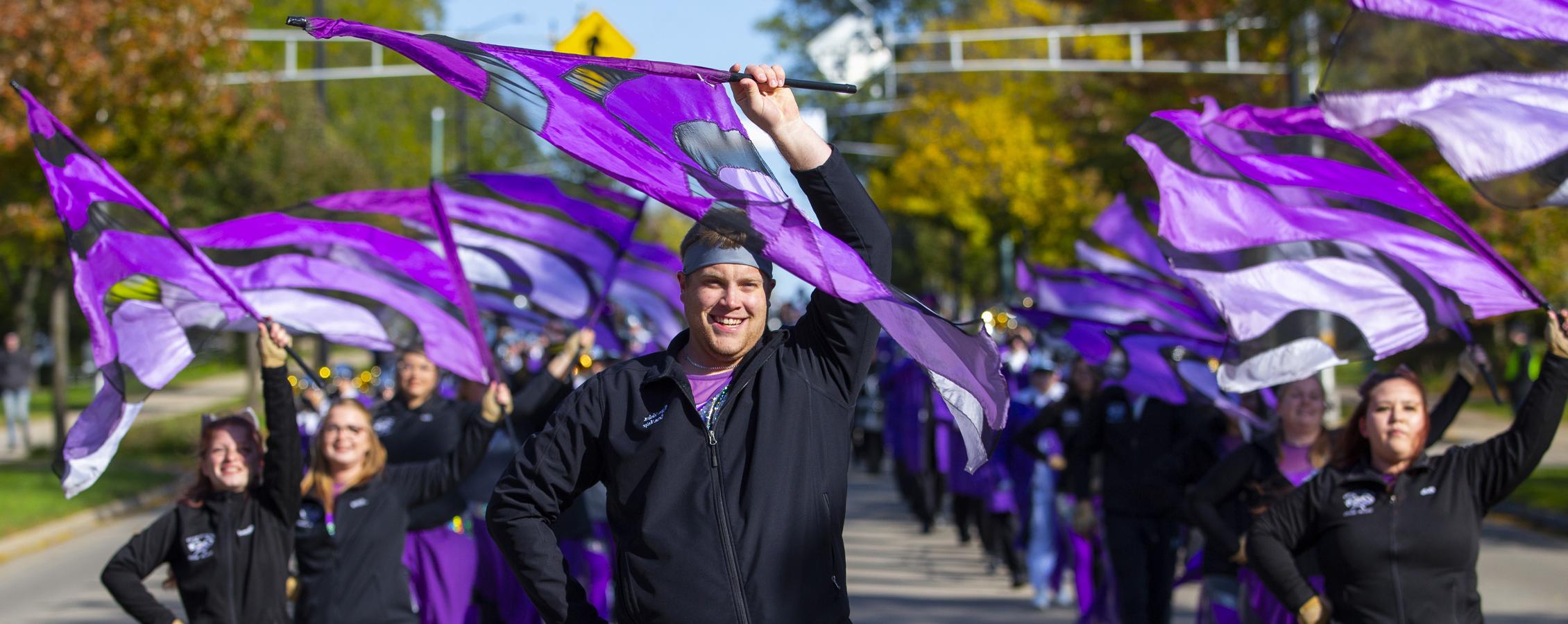 The Color Guard marches in the parade with purple flags in the air.